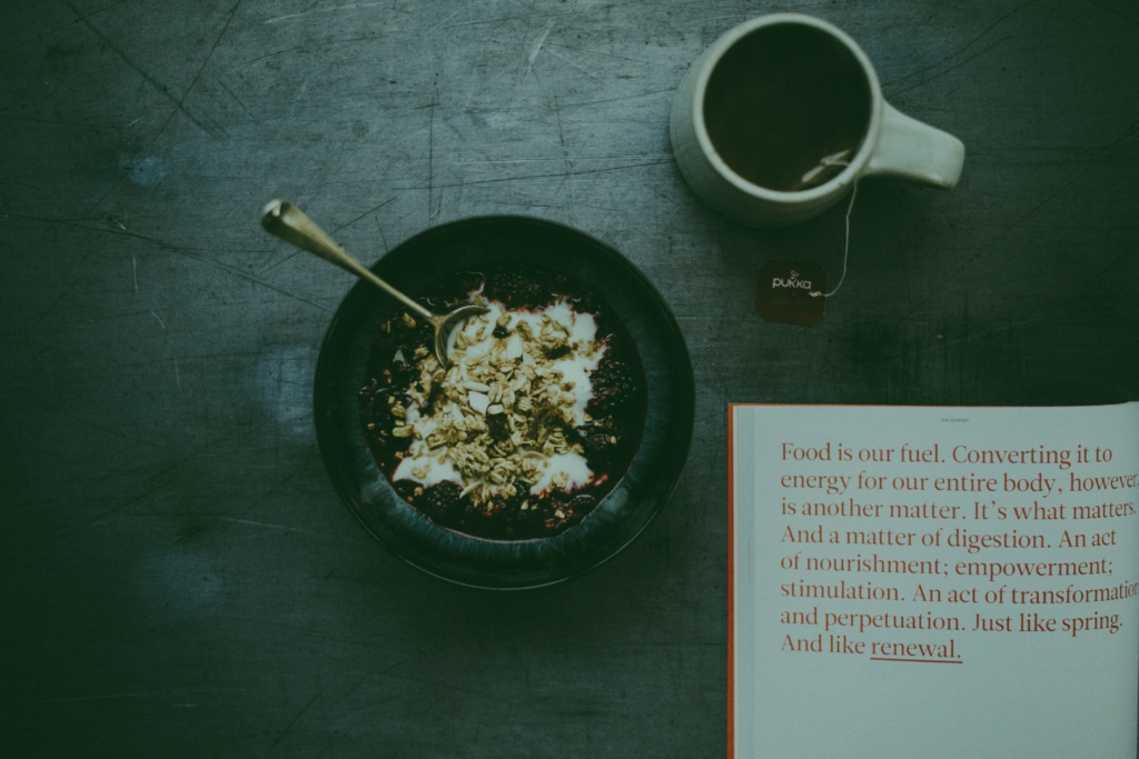 Image of Tea and cereal bowl with open book with the passage "Food is our fuel. Converting it to energy for our entire body, however is another matter. It's what matters. And a matter of digestion. An act of nourishment; empowerment; stimulation. an act of transformation and perpetuation. Just like spring. And like renewal." for "How To Release Limiting Beliefs About Our Health" blog post