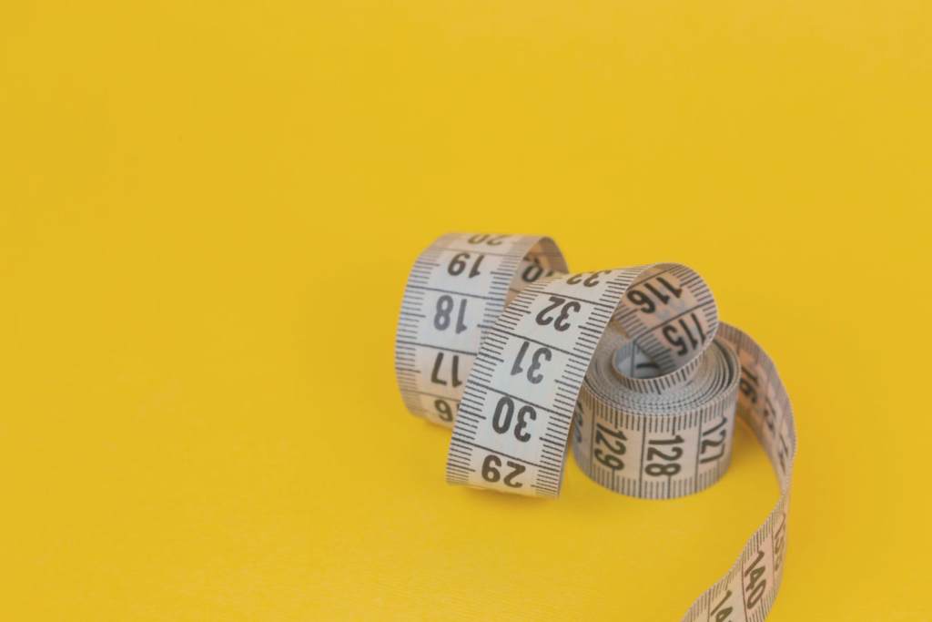 Image of measuring tape in yellow background for "Why Am I Not Losing Weight? Here's The Reason!" Blog Post